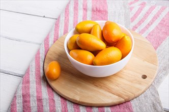 Kumquats in a white plate on a white wooden background, close up