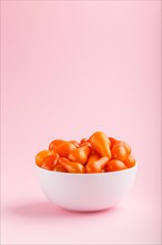 Fresh orange grape tomatoes in white ceramic bowl on pink pastel background. side view, close up,