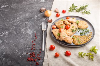 Fried pork chops with tomatoes and herbs on a gray ceramic plate on a black concrete background and