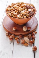 Mixed different kinds of nuts in ceramic bowl on white wooden background. hazelnut, brazil nut,