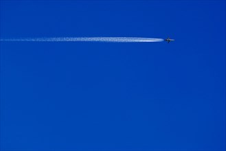 A passenger plane with vapour trail high in the blue sky