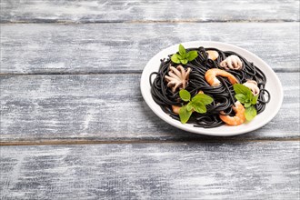 Black cuttlefish ink pasta with shrimps or prawns and small octopuses on gray wooden background.