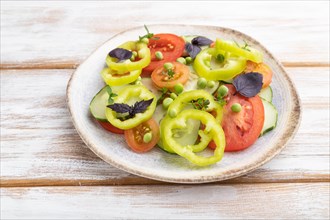 Vegetarian salad from green pea, tomatoes, pepper and basil on white wooden background. Side view,