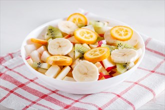 Vegetarian salad of bananas, apples, pears, kumquats and kiwi on linen tablecloth, close up,