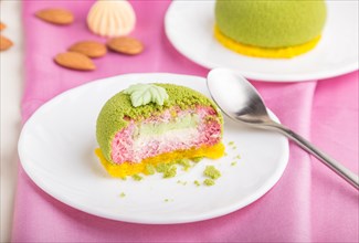 Green mousse cake with pistachio and strawberry cream on a white wooden background and pink textile