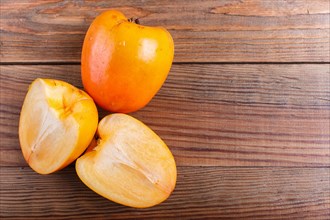 Ripe orange persimmon on brown wooden background, with copy space, top view