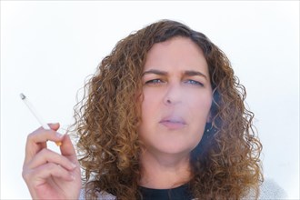 Attractive woman with long curly hair and blue eyes seen from the front smoking her cigarette