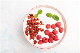 Yogurt with raspberry and goji berries in ceramic bowl on white concrete background. top view, flat