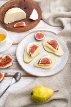 Summer appetizer with pear, cottage cheese, figs and honey on a white wooden background and linen