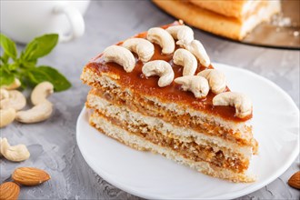Piece of homemade cake with caramel cream and nuts with cup of coffee on a gray concrete background