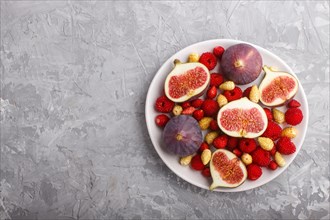Fresh figs, strawberries and raspberries on white ceramic plate on gray concrete background. top