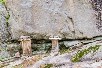 Two logs held in place with stones and carved to have one eye and mouth on rocky ledge of cliff