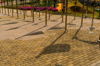 Shadows of flags on brick walkway between rows of chrome flagpoles in public park in South Korea