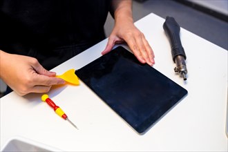 Repairman using pick to repair a digital tablet in a workshop
