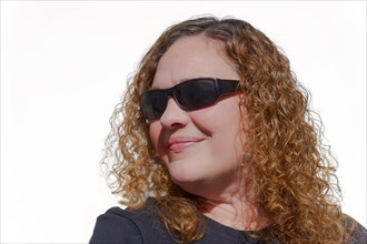 Curly-haired blonde woman seen in profile wearing sunglasses with white background and copy space