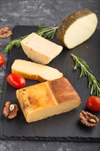 Smoked cheese and various types of cheese with rosemary and tomatoes on black slate board on a