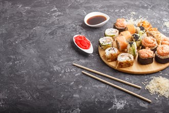 Mixed japanese maki sushi rolls set with chopsticks, ginger, soy sauce, rice on black concrete