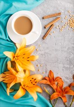 Orange day-lily and lavender flowers and a cup of coffee on a gray concrete background, with blue