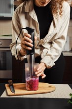 Unrecognizable woman making detox shake or smoothie at home with blender