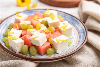 Vegetarian salad with watermelon, feta cheese, and grapes on blue ceramic plate on white wooden
