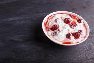 White plate with greek yogurt and strawberry jam on black wooden background.close up. copy space