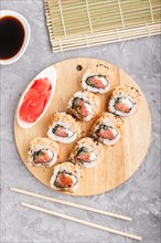 Japanese maki sushi rolls with salmon, sesame, chopsticks, soy sauce and marinated ginger on wooden
