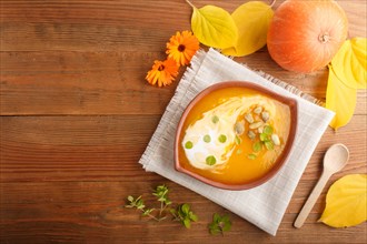 Traditional pumpkin cream soup with seeds in clay bowl on a brown wooden background with linen