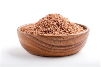 Wooden bowl with unpolished brown rice isolated on white background. Side view, close up