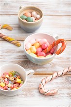 Heap of multicolored caramel candies in cups on white wooden background. side view, close up