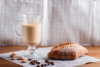 Glass cup of coffee with cream and bun on a wooden background and linen textile. close up, copy
