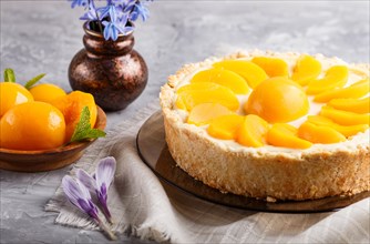 Round peach cheesecake and ceramic vase with blue flowers on a gray concrete background. side view,