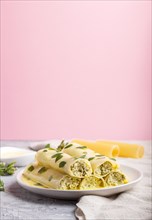 Cannelloni pasta with egg sauce, cream cheese and oregano leaves on a gray and pink background with