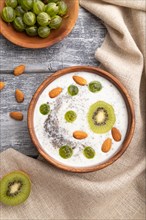 Yogurt with kiwi, gooseberry, chia and almonds in wooden bowl on gray wooden background and linen
