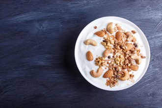 White plate with greek yogurt, granola, almond, cashew, walnuts on black wooden background. top