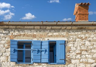 A rustic building with blue shutters under a clear blue sky with few clouds, Istria, Croatia,