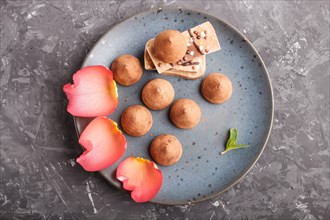 Chocolate truffle on blue ceramic plate decorated with rose petals on black concrete background.