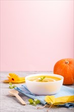 Traditional pumpkin cream soup with in white bowl on a gray and pink background with blue napkin.