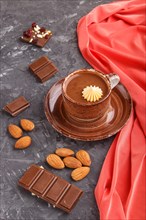 Cup of hot chocolate and pieces of milk chocolate with almonds on a black concrete background with