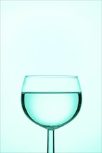 A wine glass filled with turquoise liquid against a uniform blue background