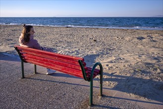 Young woman sitting on bench, bench, looking at the sea, coat, lonely, alone, beach, Peraia, also