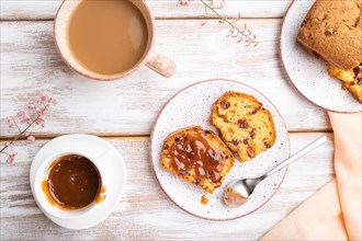 Homemade cake with raisins, almonds, soft caramel and a cup of coffee on a white wooden background