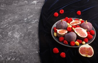Fresh figs, strawberries and raspberries on blue ceramic plate on black concrete background and