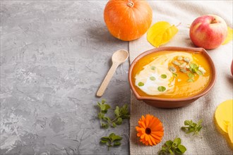 Traditional pumpkin cream soup with seeds in clay bowl on a gray concrete background with linen