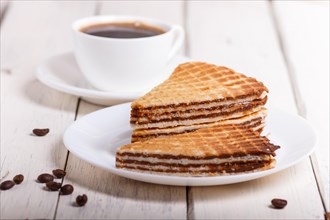 Waffle sandwiches with boiled condensed milk in plate on white wooden table with cup of coffee.