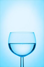 Wine glass half filled with water and a blue background