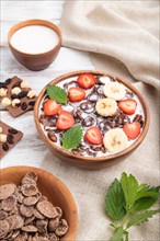 Chocolate cornflakes with milk and strawberry in wooden bowl on white wooden background and linen