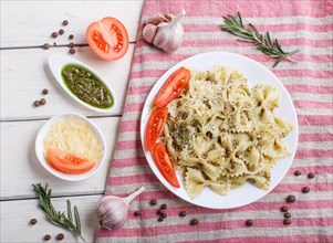 Farfalle pasta with pesto sauce, tomatoes and cheese on a linen tablecloth on white wooden