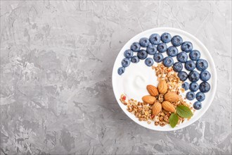 Yoghurt with blueberry, granola and almond in white plate on gray concrete background. top view,