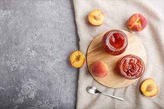 Peach jam in a glass jar with fresh fruits and linen textile on gray concrete background. top view,