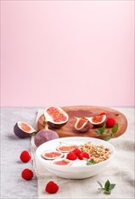 Yoghurt with raspberry, granola and figs in white plate on a gray and pink background and linen